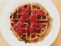 A round waffle with raspberries & maple syrup on top, fit snugly into a round plate.